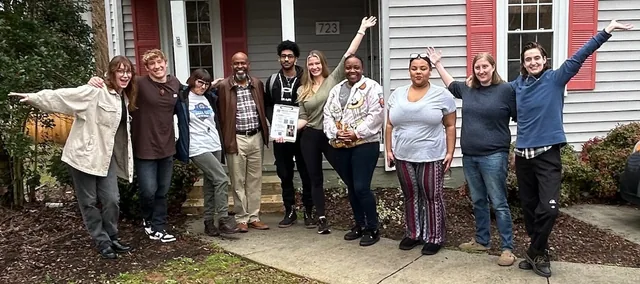 A canvassing team celebrating on the front steps of a house, arms in the air