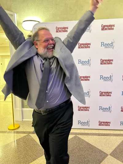 Ted, arms raised in celebration, in front of the Campaigns & Elections Reed Awards backdrop