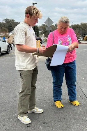 A young canvasser collecting a voter's first signature on a clipboard in a parking lot